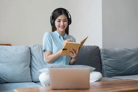 Woman taking notes in notebook while using laptop at home in living room 库存照片
