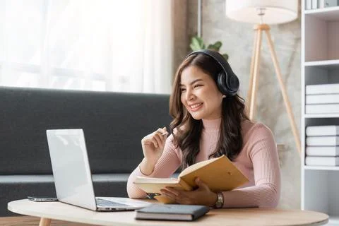 Woman taking notes in notebook while using laptop at home in living room 写真素材