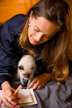 Woman taking notes while a siamese kitten climbs on her lap Stock Photos