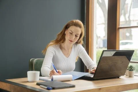 Woman Taking Notes While Working on Laptop Planning and Productivity Concept 스톡 사진