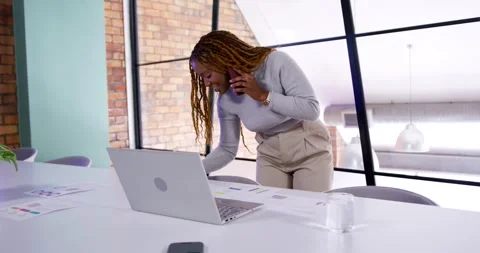Woman taking phone call while leaning over table, using laptop and reviewing Stock Footage 341865256