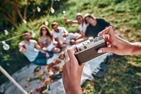 Woman taking picture of her friends by vintage camera on picnic at summer par Stock Photos