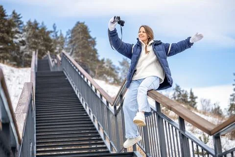 Woman taking selfie with camera while balancing on stair railing in winter,.. Stock Photos