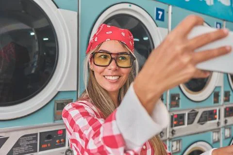 Woman taking selfie while doing laundry at laundromat Stock Photos