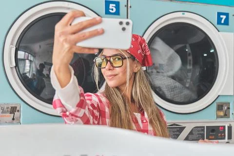 Woman taking selfie while doing laundry at laundromat Stock Photos