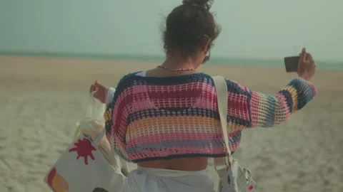 Woman Taking Selfie While Walking on Sandy Beach With Bags and Sunglasses Stock Footage 338403667