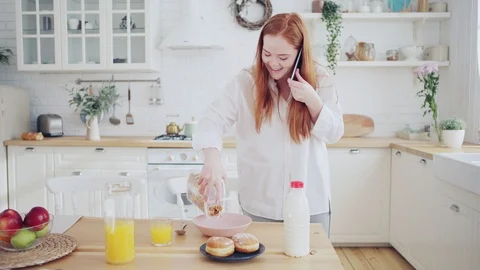 Woman talking on cell phone while preparing breakfast Stock Footage 106306190
