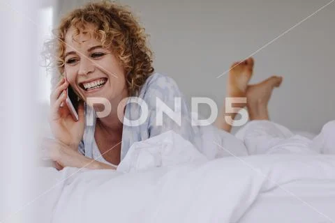Woman talking on mobile phone lying on bed Stock Photos