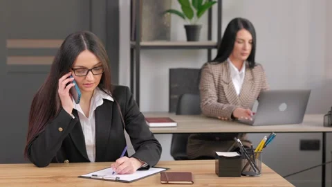 Woman talking on mobile phone while sitting on a desk Stock Footage 318528437
