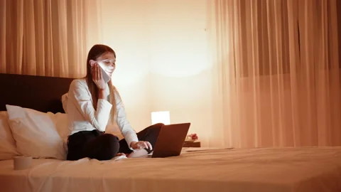 Woman talking on mobile while sitting on bed with laptop Stock Footage 164970893