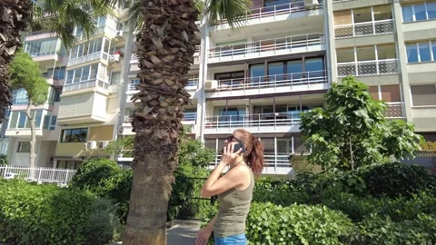 Woman talking on phone while walking among palm trees on sunny day. Stock Footage 219848465