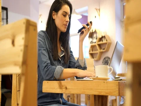 Woman talking on phone while working at coffee shop table Stock Footage 82947517