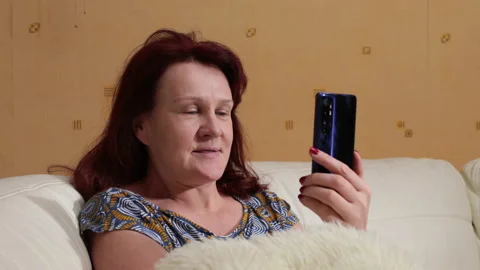 Woman is talking on a video call using her smartphone. She sits on the couch Stock Footage 145478120