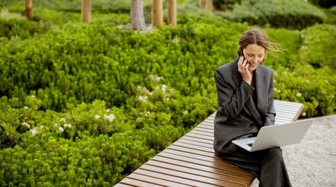 Woman talks on phone while working on laptop in garden Stock Photos