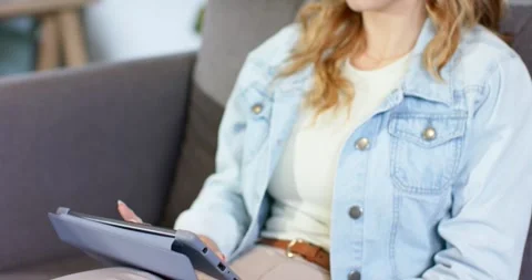 Woman tapping and scrolling tablet wearing smartwatch on sofa at home, smiling Stock Footage 336174324
