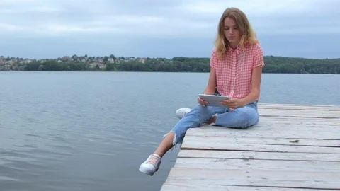 Woman tapping at tablet while sitting near lake in slow motion Stock Footage 91726185