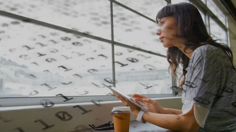 Woman tapping tablet at window counter, summoning binary overlay while working, Stock Footage 333720005