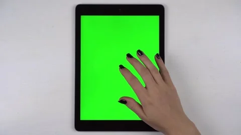 A woman taps on a tablet lying on a table with a green screen. A woman's hand is Stock Footage 218509155