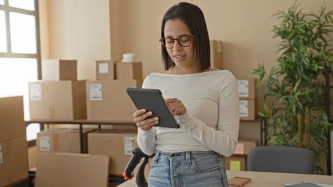Woman taps tablet while standing amid packed parcels and boxes in a buildin.. Stock Footage 339231506
