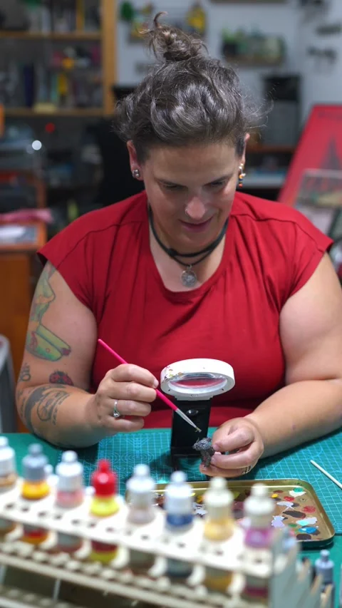 Woman with tattoos smiling while meticulously painting a miniature figurine 動画素材 342923231