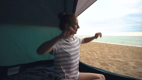 Woman in tent in the wilderness looking at sunrise at sea shore in the morning Stock Footage