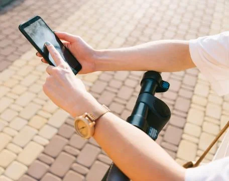 Woman texting message on smartphone while standing with an electric scooter. Stock Photos
