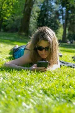 Woman texting in a smart phone relaxed in the country with a green field in t Stock Photos