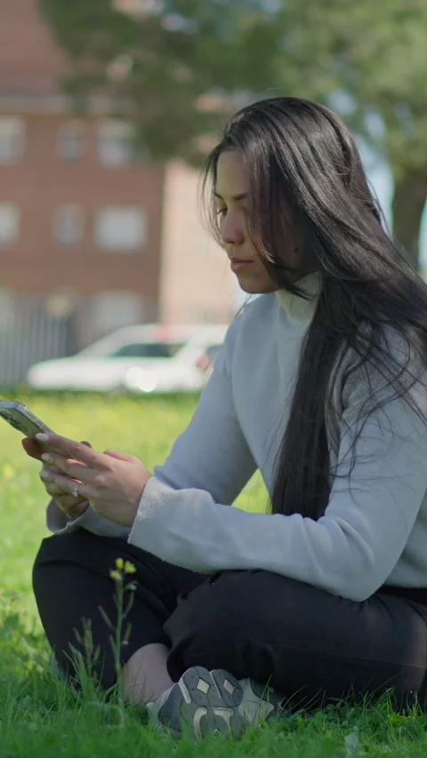 Woman texting on smartphone while sitting on green grass in city park Stock Footage 332790620