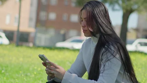 Woman texting on smartphone while sitting on green grass in city park Stock Footage 332790621