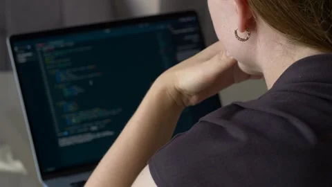 Woman thinking while looking at programming code on laptop with hand near face Stock Footage 345652338
