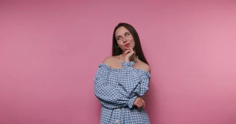 Woman thinks while posing against a pink background in a studio setting dur.. Stockbeeldmateriaal 331990033