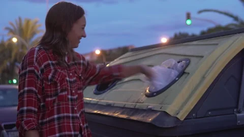 Woman throwing garbage into garbage can in the evening Stock Footage 254069720