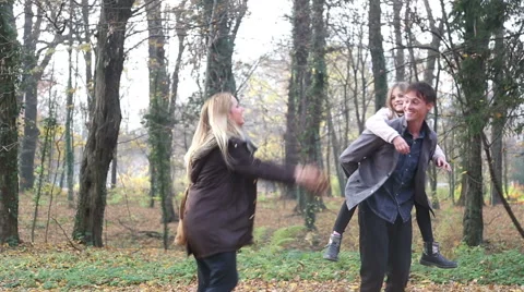 Woman throwing leaves at her daughter and husband in the park Stock Footage 59553945