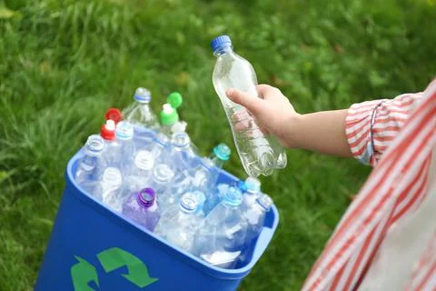 Woman throwing used bottle into trash bin outdoors, closeup. Plastic recyclin Stock Photos