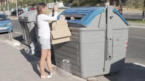 A woman throws corton boxes into a special garbage can on the street Stock Footage 252821292