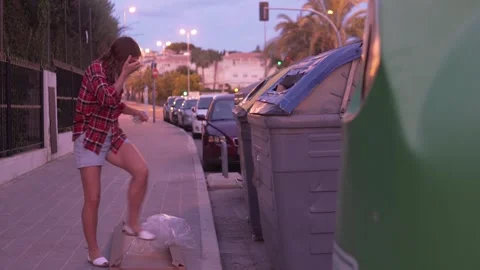 A woman throws garbage into a trash can on the street in the evening Stock Footage 254171039