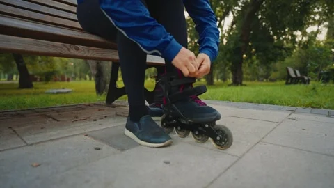 Woman ties roller skates while preparing for outdoor skating in the park 스톡 동영상 284408300