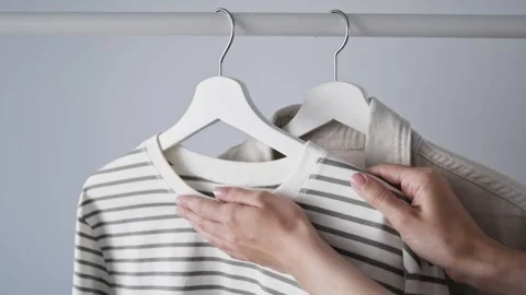 Woman touches light-colored striped vest hanging on white wooden hanger Stock Footage 340266509