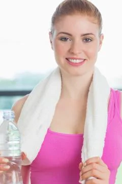 Woman with towel around neck holding water bottle in fitness studio Stock Photos