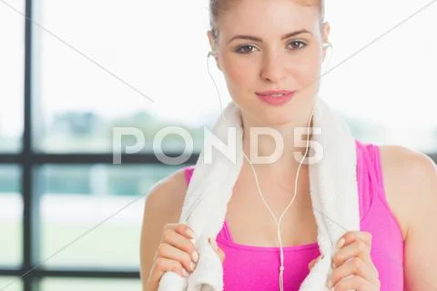 Woman with towel around neck listening to music in fitness studio Stock Photos