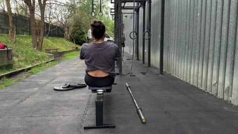 Woman training on rowing machine in outdoor gym with calisthenics equipment, fit Stock Footage 334580020