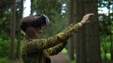 Woman tries to catch virtual objects playing with VR headsetin a forest Stock Footage 80130817