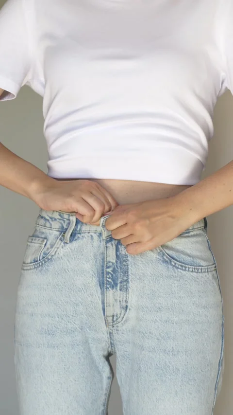 Woman trying to button tight jeans. Close-up of female body struggling with Stock Footage 336408053
