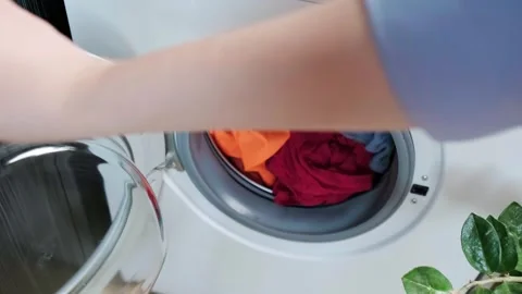 Woman turning on washing machine, loading clothes for washing, concept of laundr Stock Footage 295286804