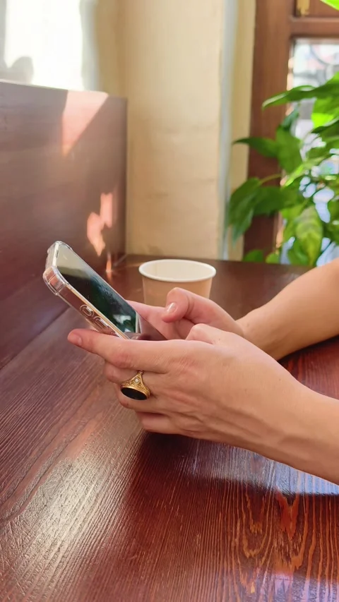 Woman types message on smartphone sitting at cafe table with coffee cup Stock Footage 337346558