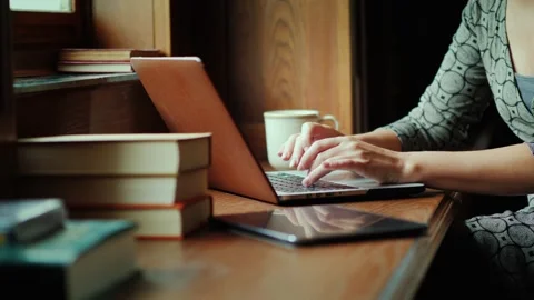 Woman typing on a laptop computer while sitting by a window in a cozy study.. Stock Footage 334607101