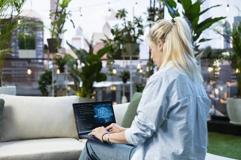 Woman typing on laptop displaying code and digital AI graphic from rooftop Stock Photos
