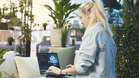 Woman typing on laptop displaying code and digital AI interface from rooftop Stock Photos