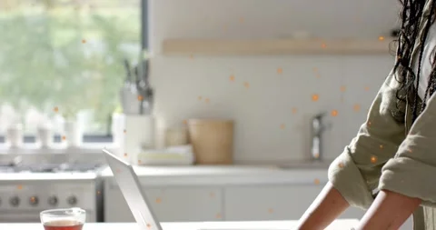 Woman typing on laptop in kitchen, orange flecks appearing and highlighting Stock Footage 320896053