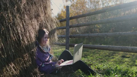 Woman typing on laptop under a stack of hay Stock Footage 273591135